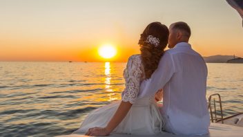 Brautpaar sitzt auf Vordeck der Segelyacht und beobachtet den Sonnenuntergang
